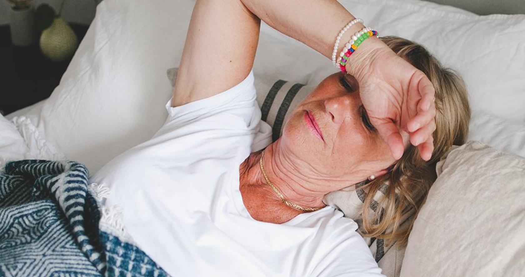 Older adult woman feeling fatigued lying down in bed