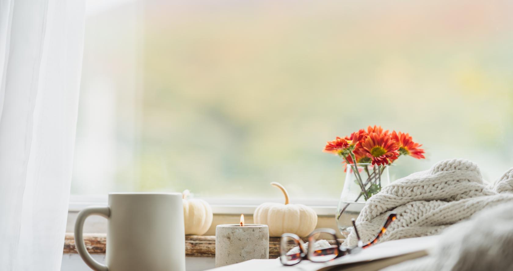 cozy interior shot of a book and blanket on a chair or couch, with a mug of tea/coffee nearby